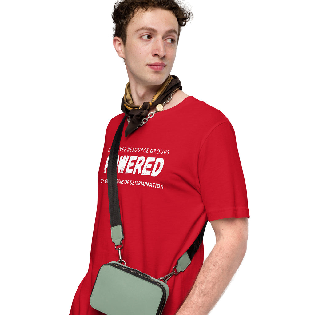 Young man with a brown and gold scarf and gold chanin around his neck  wearing a  small gray bag with black strap across his body, wearing a red t-shirt with the words Employee Resource Groups Powered by Generations of Determination across the front