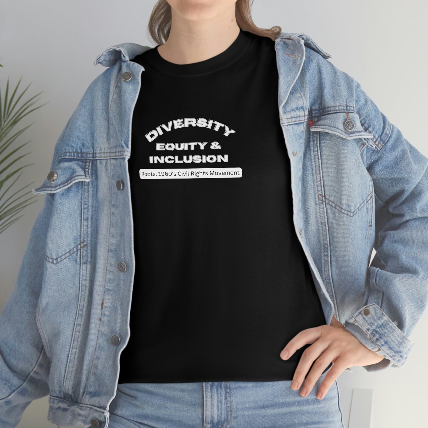 Female Model wearing black t-shirt with lettering In bold capital white letters on the front "Diversity Equity & Inclusion" below these letters on a rounded white background strip with mixed case black letters "roots: 1960's Civil Rights Movment" under a light colored denim jacket